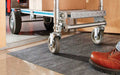 Insitu image of grey SmartGrip Roll Mat with a trolley rolling over it in a workplace to transport packages.