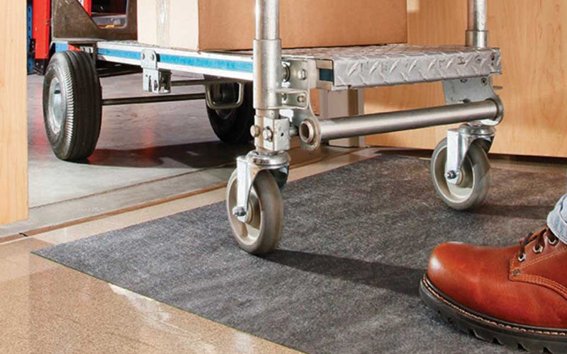 Insitu image of grey SmartGrip Roll Mat with a trolley rolling over it in a workplace to transport packages.